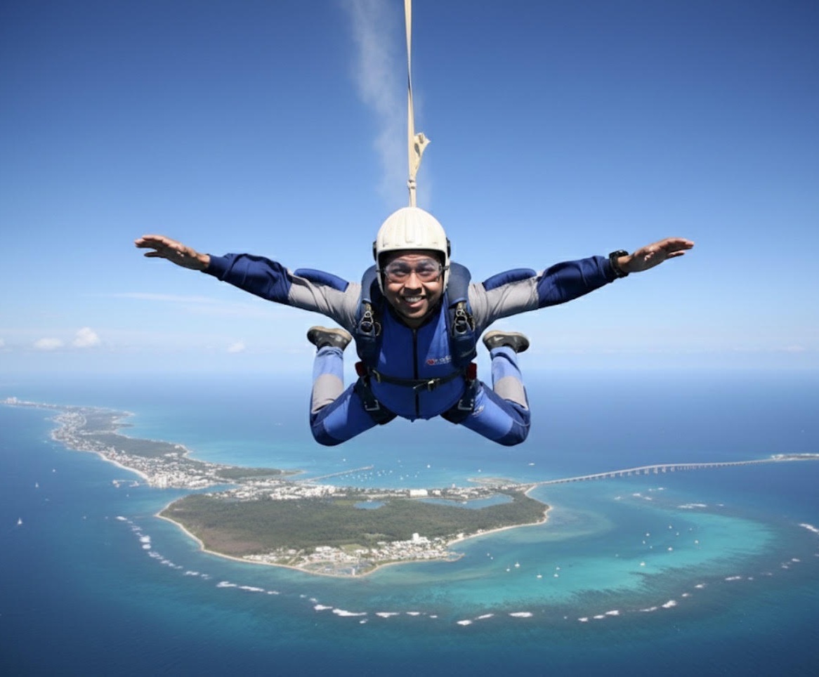 Nur Al Faisal in freefall during a skydive, arms spread, over an island coastline and blue sea